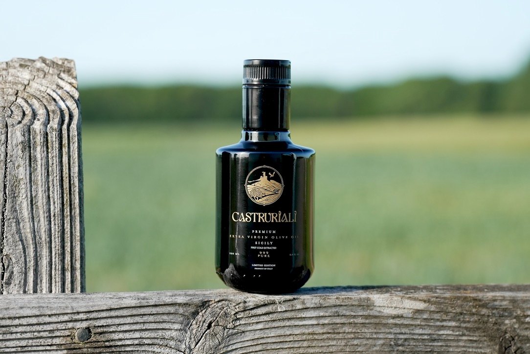 A bottle of Castruriali on a weathered fence post above the Sicilian fields