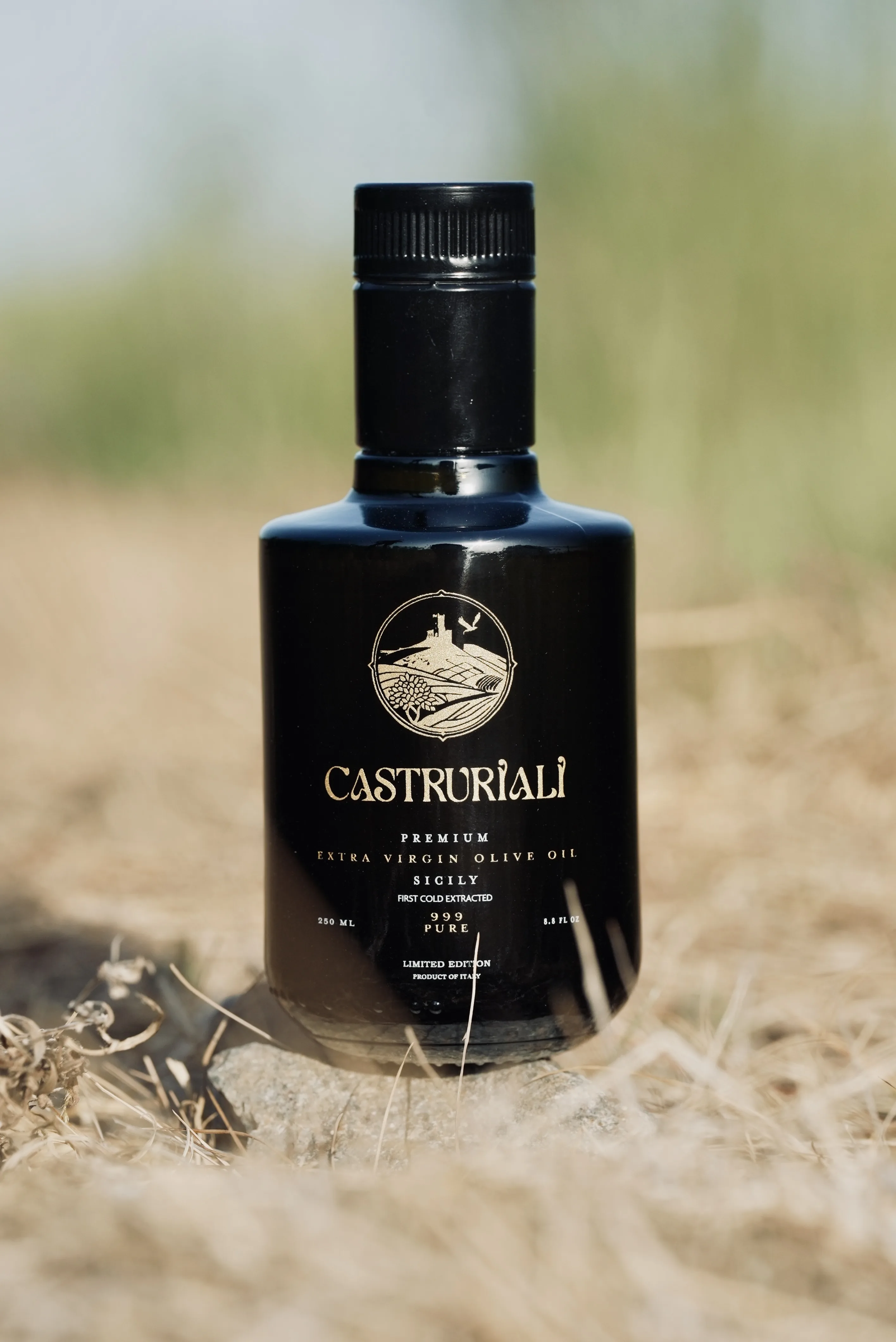 A bottle of Castruriali extra virgin olive oil standing in a sunlit Sicilian field